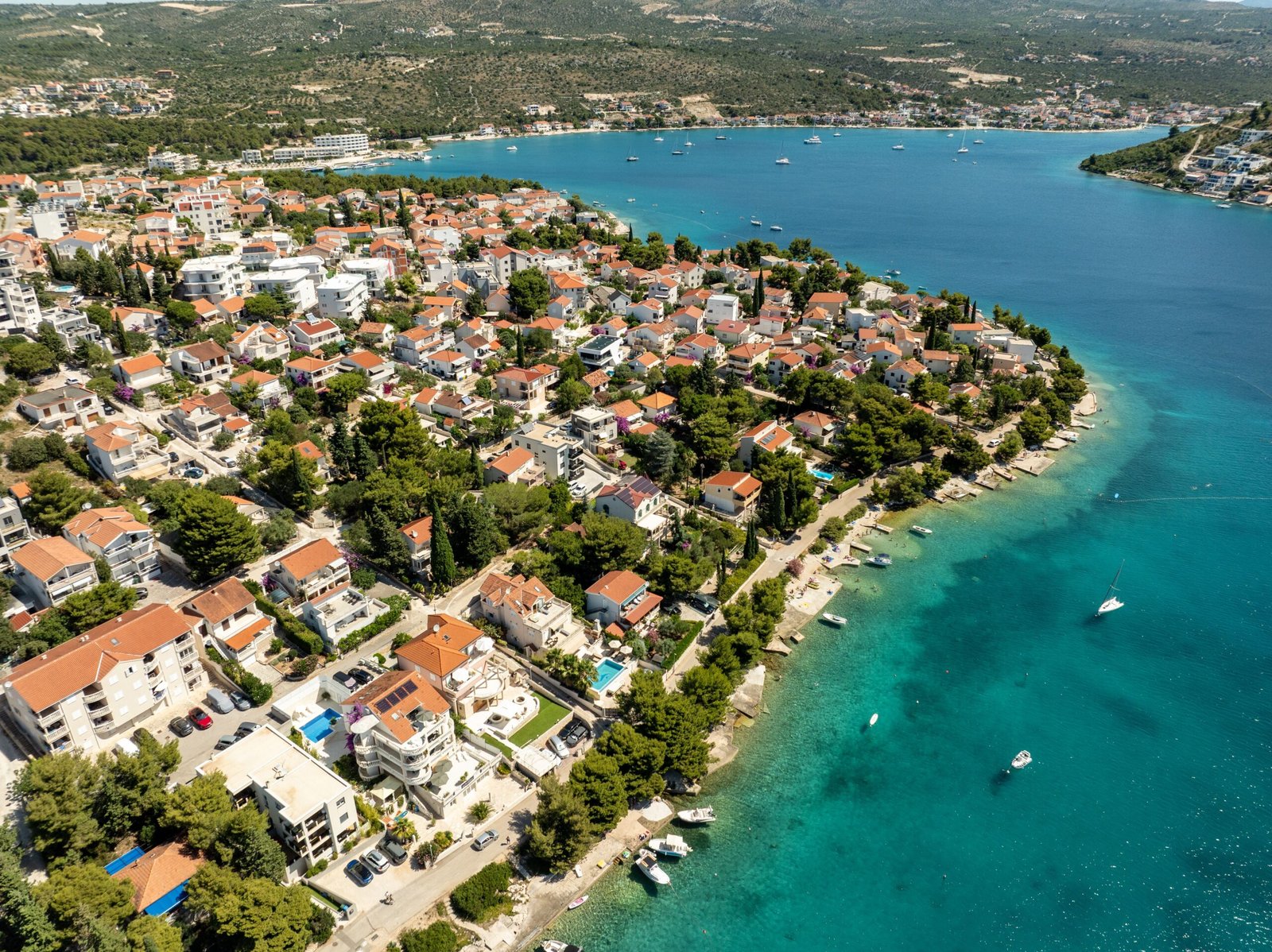 Aerial view of a coastal town with red-roofed houses lining a peninsula beside turquoise sea and boats